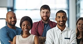 A diverse team of people stand in front the camera, smiling.